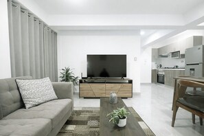Una sala moderna con un sofá, televisión, mueble de madera y un comedor con mesa y sillas.