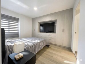 A bedroom with a bed, a TV mounted on the wall, a desk with a lamp, and a window with blinds. - Apartment in Yanahuara: Modern, Central, and Fully Equipped (Yanahuara)