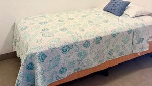 Una cama individual con colcha estampada, una almohada azul y una almohada blanca sobre un cabecero de madera.