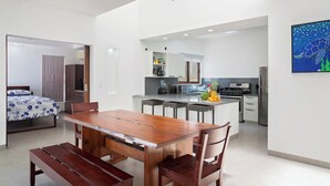 Una cocina moderna con una isla central, un comedor con una mesa de madera y bancos, y un dormitorio con cama y armario.