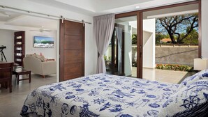 Un dormitorio con una cama grande, un escritorio, una silla, un televisor y una puerta corrediza de vidrio que da a un balcón.