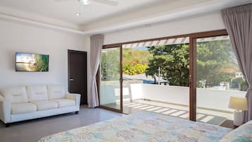 Habitación de hotel con cama, sofá, ventilador de techo, un cuadro y balcón con cortinas.