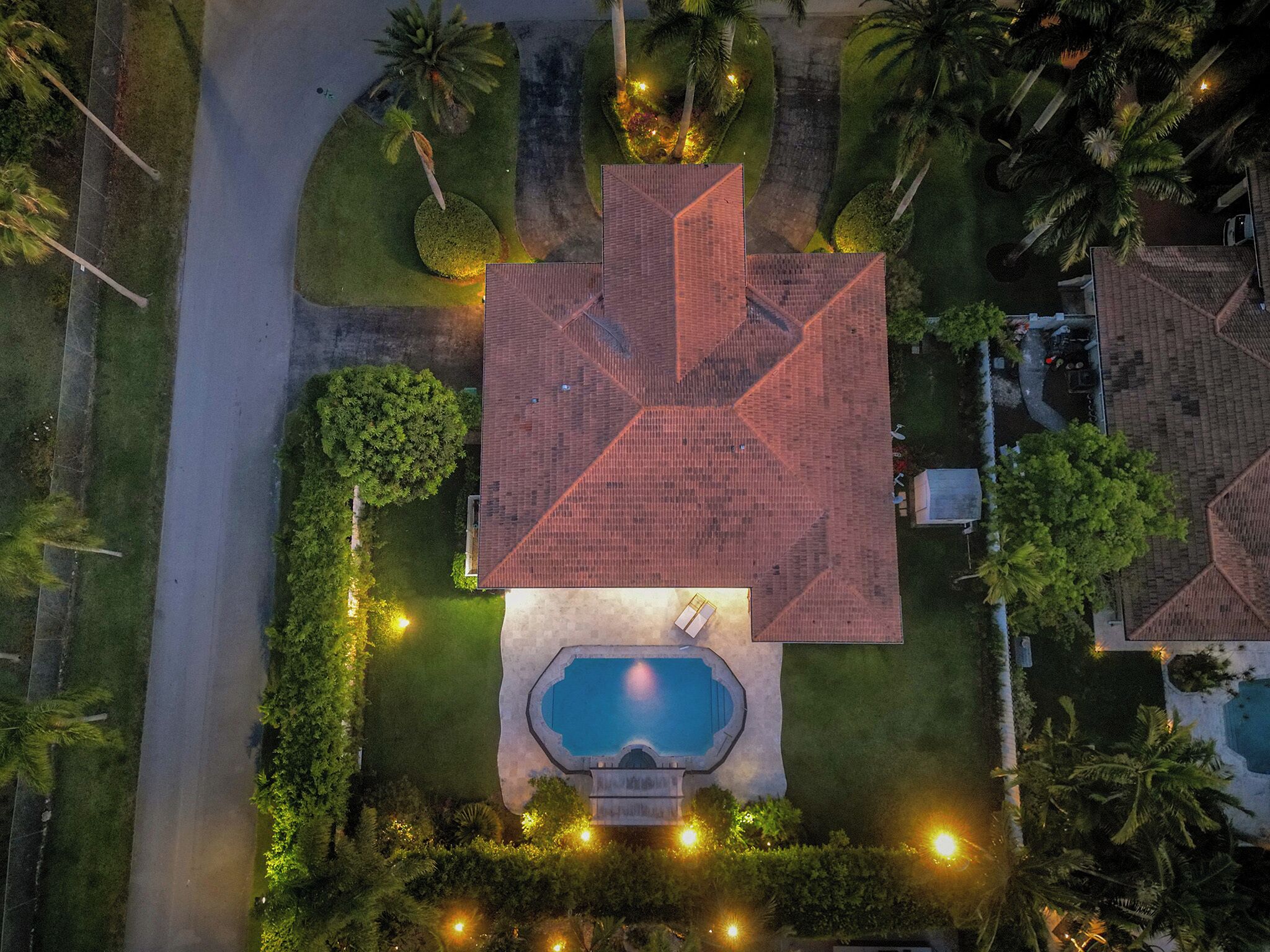 An aerial view of a residential property with a swimming pool, surrounded by well-maintained lawns and palm trees.
