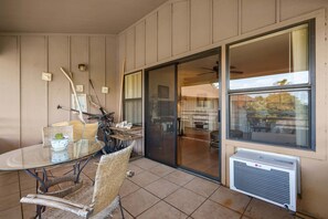 Eine überdachte Terrasse mit einem Glastisch, Korbstühlen und einer Klimaanlage.