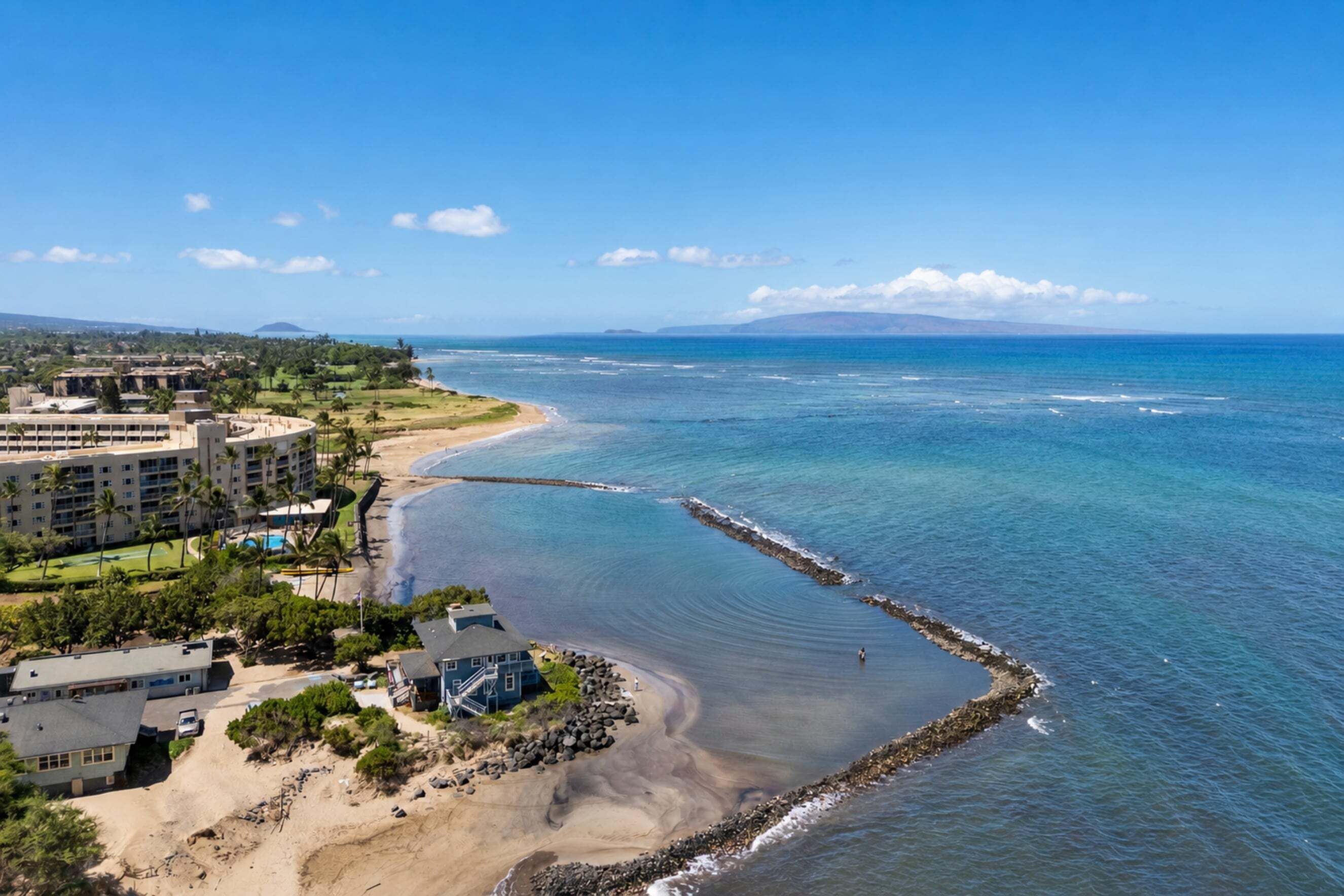 A coastal hotel with a beachfront view, a swimming pool, and a rocky shoreline.