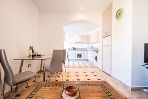 A narrow hallway with a dining table and chairs, a kitchen area with a washing machine, and a clock on the wall. - Sunrays Naturist Apartment in Playas de Vera (Vera)