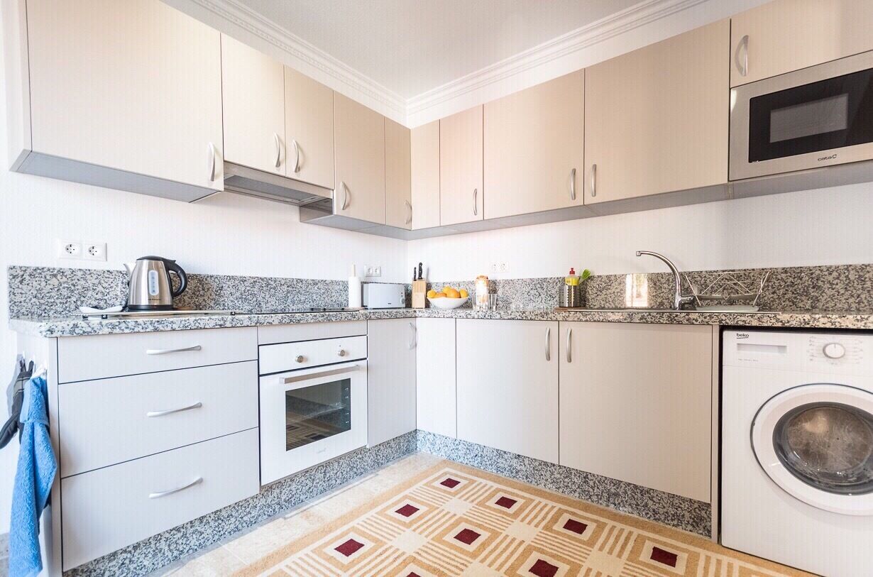 A compact kitchen with white cabinets, a built-in oven, a microwave, and a washing machine.