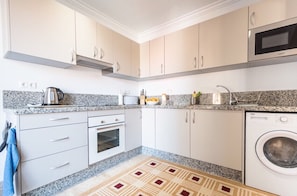 A compact kitchen with white cabinets, a built-in oven, a microwave, and a washing machine. - Sunrays Naturist Apartment in Playas de Vera (Vera)
