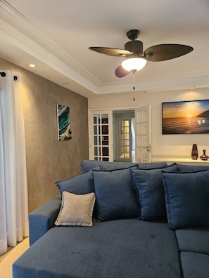 A modern living room with a sectional sofa, a ceiling fan, and a painting of a sunset. - Cozy beachfront apartment in Module 2 (Riviera de São Lourenço)