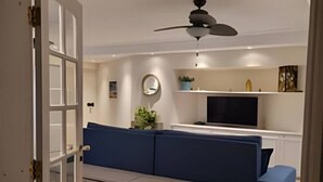 Un salon comprenant un canapé, un téléviseur, un ventilateur de plafond et une porte donnant sur une autre pièce.