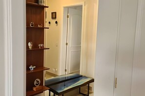 A hallway with a wooden shelf unit, a glass table, and a white door. - Cozy beachfront apartment in Module 2 (Riviera de São Lourenço)