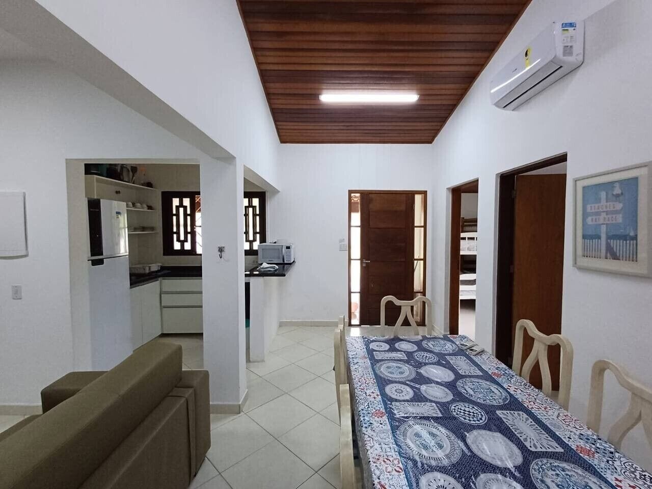 A room with a dining table, chairs, a sofa, a kitchen area, and a ceiling fan.