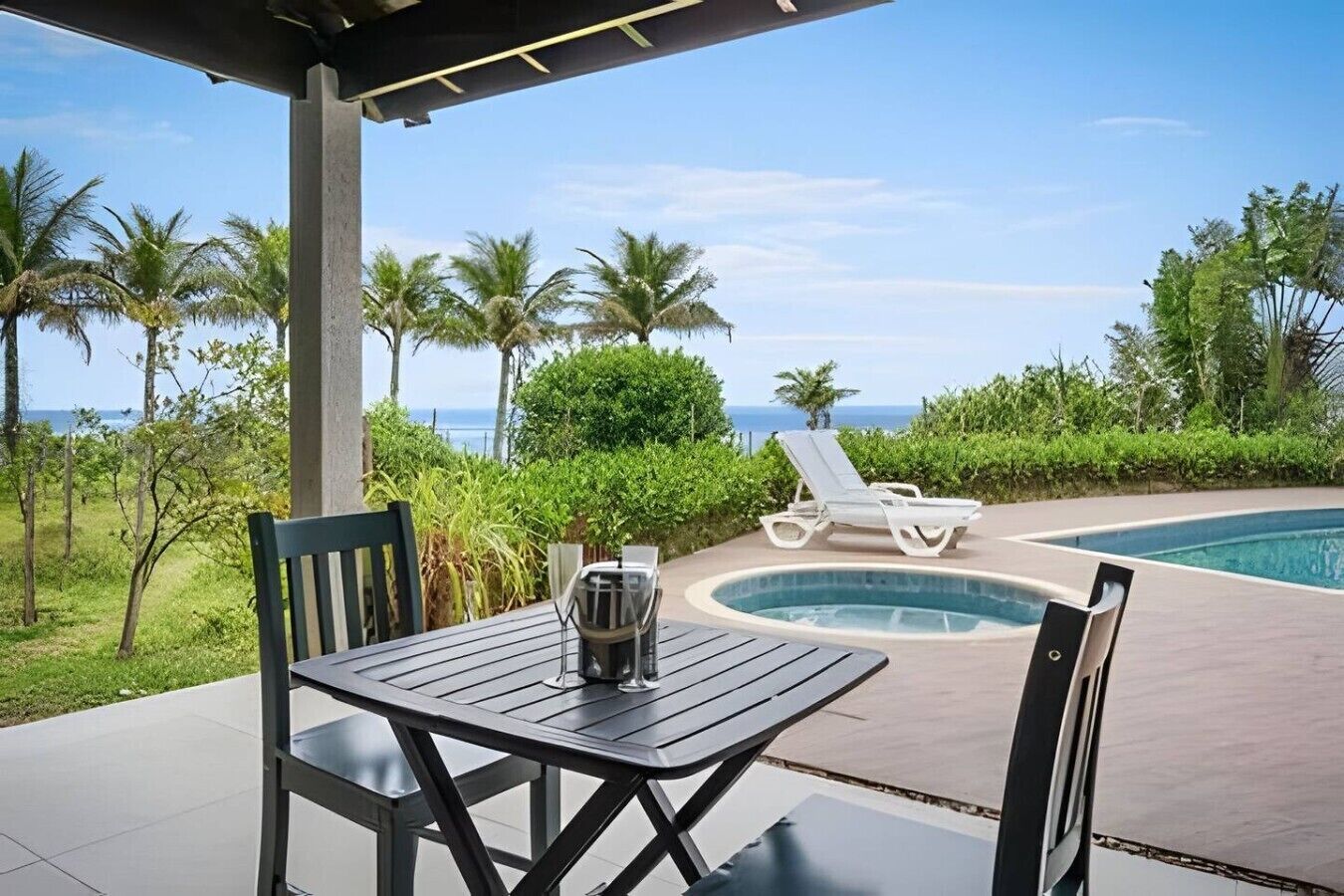 A poolside area with a table, chairs, and a view of the ocean.