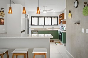 A modern kitchen with a central island, pendant lighting, and a view to the outside. - Beachfront with pool - Costa do Sol (Loteamento Costa do Sol)