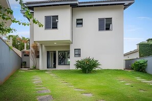 A two-story building with a flat roof, a small front porch, and a well-maintained lawn with stepping stones. - Beachfront with pool - Costa do Sol (Loteamento Costa do Sol)