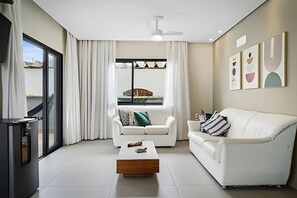 A modern living room with a white sofa, a coffee table, and a TV on a stand. - Beachfront with pool - Costa do Sol (Loteamento Costa do Sol)