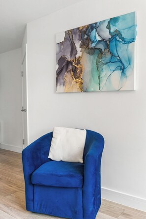 A room with a blue armchair, a white cushion, and a large abstract painting on the wall. - Penthouse for 8, Roof Terrace, 9 Min Drive to Studio Tour (Hertfordshire)