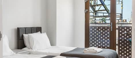 A modern bedroom with two beds, a large window, and a view of an industrial area.