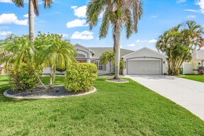 A residential area with houses, a well-maintained lawn, and palm trees. - Envision Paradise: Gorgeous 4 Bedroom Waterfront Home with Private Pool/Spa and Large Kitchen (Cape Coral)