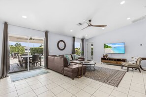 A modern living room with a sofa, coffee table, TV, and a ceiling fan. - Envision Paradise: Gorgeous 4 Bedroom Waterfront Home with Private Pool/Spa and Large Kitchen (Cape Coral)