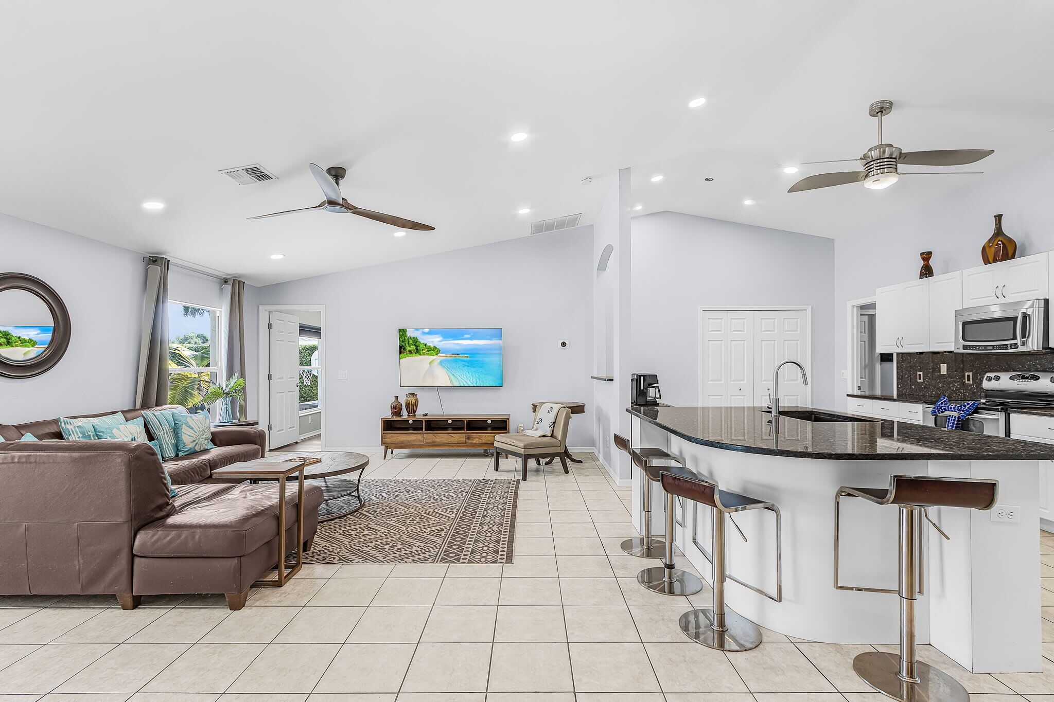 A modern kitchen with a central island, bar stools, and a dining area with a sofa and coffee table.