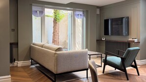 A modern living room with a sofa, two chairs, a TV, and a large window with a view of a tree. - Terrific 2-bedroom apartment in central London perfect for your stay (London)