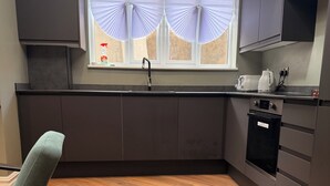 A modern kitchen with dark cabinetry, a herringbone wood floor, a window with sheer curtains, and a built-in oven. - Terrific 2-bedroom apartment in central London perfect for your stay (London)