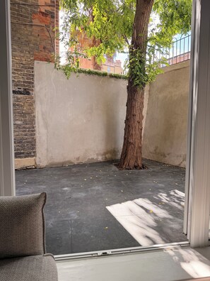 Um quarto com piso de concreto, uma árvore e uma parede de tijolos.