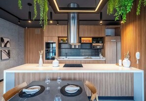 A modern kitchen with a central island, wooden cabinetry, and hanging plants. - Luxury Stay Steps from Larcomar | Pool & Parking (Miraflores)
