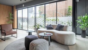 Een moderne woonkamer met een bank, voetenbankje en stoel, een ronde salontafel en grote ramen met uitzicht op het omliggende landschap.