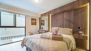Een moderne slaapkamer met een groot bed, een nachtkastje, een spiegel en een raam met balkon.