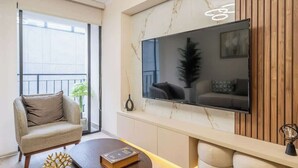Een moderne woonkamer met een bank, een salontafel, een flatscreen televisie bevestigd aan een marmeren muur, en een balkon met een leuning.