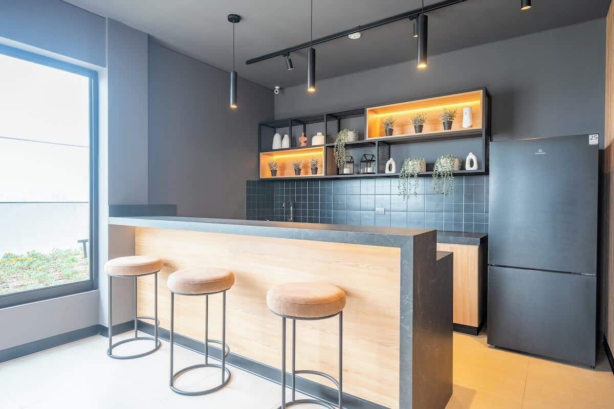 A modern kitchen with a bar area, built-in shelves with plants, and a large window.
