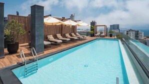 A rooftop pool with lounge chairs and umbrellas, surrounded by wooden panels and a city view. - Steps from Larcomar | 3BR · A/C · Parking (Miraflores)