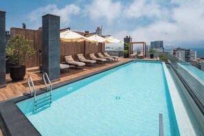 A rooftop pool with lounge chairs and umbrellas, surrounded by wooden panels and a city view. - Steps from Larcomar | 3BR · A/C · Parking (Miraflores)
