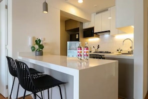 Eine moderne Küche mit weißen Schränken, einer zentralen Kochinsel mit Barhocker, einem Kühlschrank und einer Mikrowelle.
