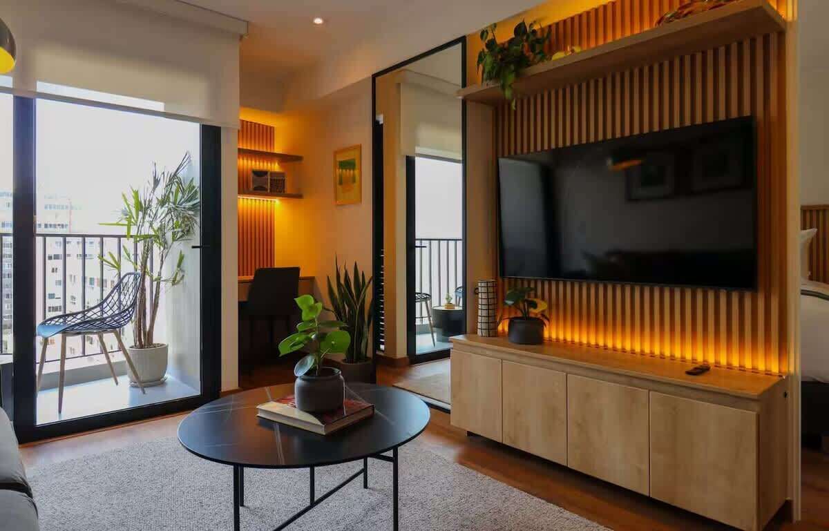 A modern living room with a large TV, a sofa, a coffee table, and a balcony with plants.