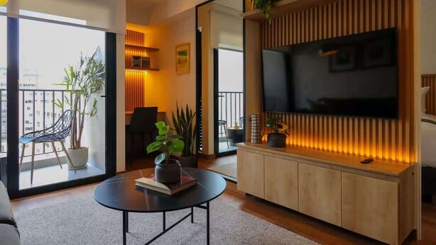 En moderne stue med stort tv, sofa, sofabord og en balkon med planter.
