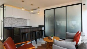 Et moderne køkken med en bar, et opholdsområde med sofa og stole, og en stor skydedør af glas.