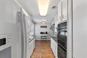 Eine schmale Küche mit weißen Schränken, einem Kühlschrank, einem Backofen und einer Mikrowelle.