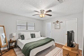 Ein Schlafzimmer mit einem Bett, einem Deckenventilator, einem Fernseher und einer Tür mit einem Schild.
