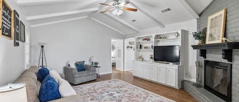 A spacious living room with a high ceiling, a fireplace, a television, and a cozy seating area.
