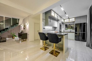 A modern kitchen with a marble countertop, two black bar stools, and a staircase with a striped railing. - Beachfront Villa Crystal Bay with Pool (Čara)