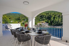 A dining area with a table set for four, surrounded by wicker chairs, overlooking a coastal landscape. - Beachfront Villa Crystal Bay with Pool (Čara)