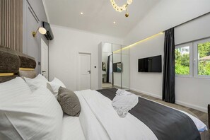 Een moderne slaapkamer met een bed, een televisie, een spiegel en een raam met uitzicht.