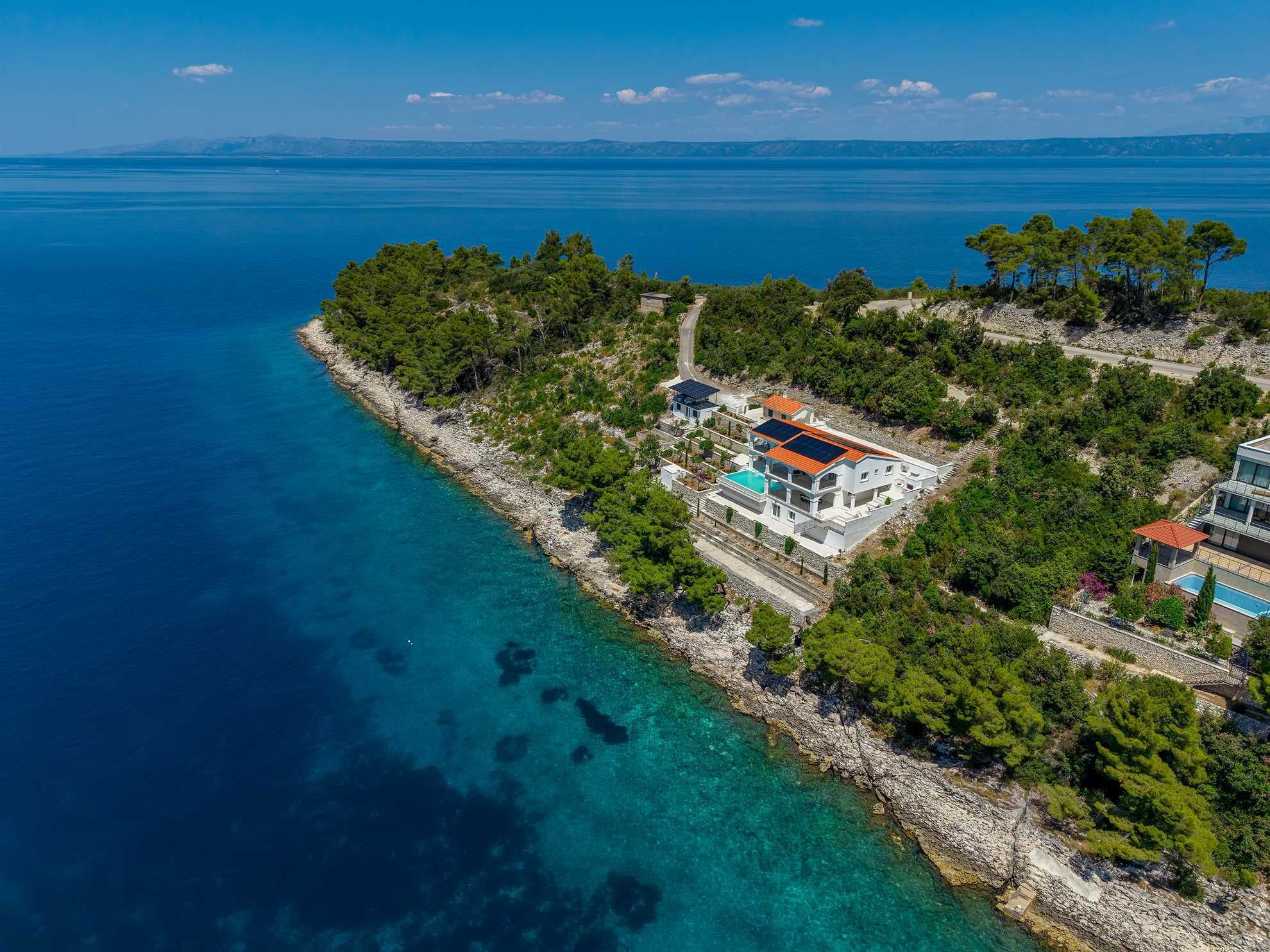 An aerial view of a coastal property with a rocky shoreline, clear blue waters, and lush greenery.