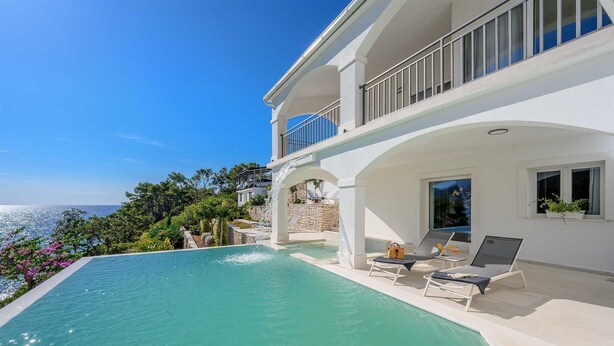 Una villa moderna con piscina, mobiliario de exterior y vista al mar.