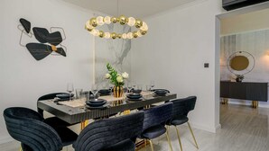 Un comedor con pared de mármol, una araña y sillas modernas.