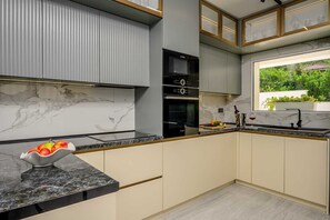 A modern kitchen with a marble backsplash, built-in appliances, and a view of greenery outside. - Beachfront Villa Crystal Bay with Pool (Čara)