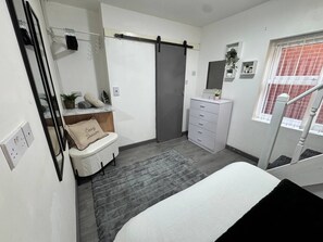 A bedroom with a bed, a dresser, a vanity with a mirror, a shower curtain, and a window with a view. - Flat a 5 Minutos do Estádio (Liverpool)